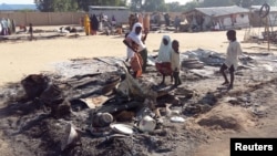 FILE - People stand amid the damage at a camp for displaced people after an attack by suspected Boko Haram insurgents in Dalori, Nigeria, Nov. 1, 2018. 