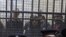 Policemen sit in front of a cage holding Egyptian employees of several pro-democracy groups during court proceedings in Cairo, Egypt, Sunday, February 26, 2012.