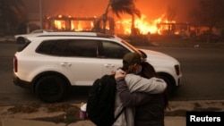 Personas se abrazan mientras evacúan luego de que los fuertes vientos alimentaron incendios forestales devastadores en el área de Los Ángeles. Foto captada en Eaton, Altadena, California, el 8 de enero de 2025.