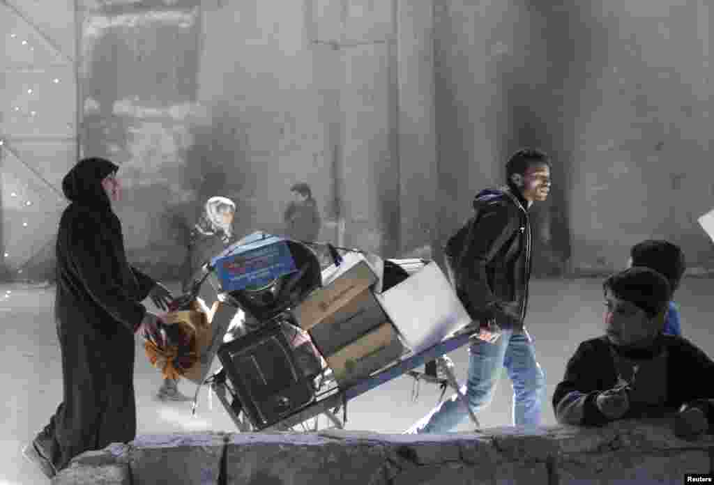 A man pulls a trolley as a woman walks behind at the Karaj al-Hajez crossing, a passageway separating Aleppo&#39;s Bustan al-Qasr, which is under the rebels&#39; control and Al-Masharqa neighborhood, an area controlled by the regime, Feb. 4, 2014.