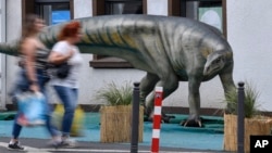 FILE - Pedestrians pass a life-size replica of a Plateosaurus dinosaur in the city center of Bochum, Germany, Monday, Aug. 12, 2019. (AP Photo/Martin Meissner)