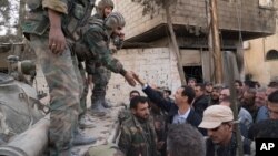 Syrian President Bashar al-Assad reaches out to shake the hand of a Syrian army soldier in eastern Ghouta, Syria, March 18, 2018.