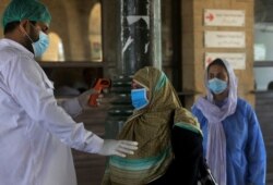 FILE - A railway worker checks the body temperature of a woman wearing a protective mask to help curb the spread of the coronavirus, on her arrival at a railway station in Karachi, Pakistan, Jan. 6, 2020.