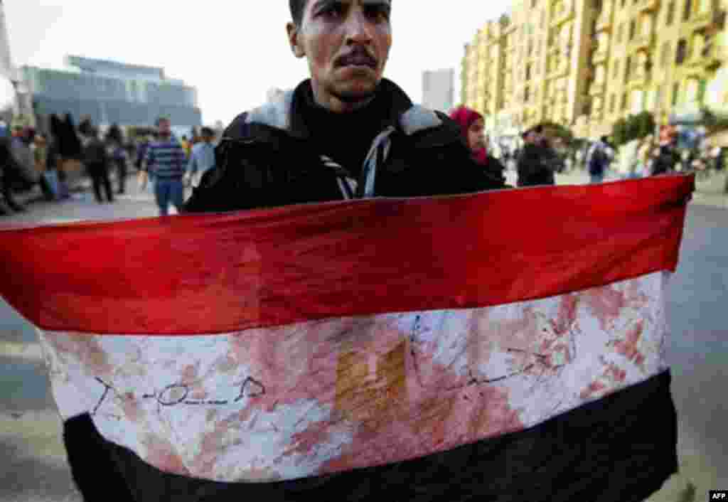 An anti-government protester displays an Egyptian flag, covered with blood, during clashes in Tahrir, or Liberation square, in Cairo, Egypt, Wednesday, Feb. 2, 2011. Several thousand supporters of President Hosni Mubarak, including some riding horses and 