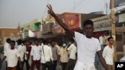 A protester flashes the victory sign, as others block a road during a protest, in Khartoum, Sudan, June 24, 2019. 