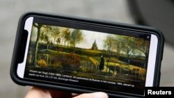 FILE - A person holds a mobile phone showing "The Parsonage Garden at Nuenen in Spring 1884," a painting by Vincent Van Gogh that was stolen, outside the Singer Laren Museum, where it was displayed, in Laren, Netherlands, March 30, 2020. 