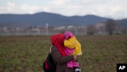 Une femme porte un bébé au poste de la frontière grecque nord de Idomeni , le vendredi 4 Mars 2016. (AP Photo/Vadim Ghirda)