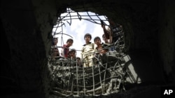 FILE - Boys look through a hole made by a Saudi-led airstrike on a bridge in Sanaa, Yemen, March 23, 2016. 