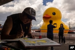 People take picture of an art installation called "Double Ducks" by Dutch artist Florentijn Hofman at Victoria Harbour in Hong Kong, Friday, June 9, 2023. (AP Photo/Louise Delmotte)