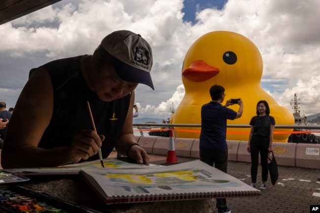 People take picture of an art installation called "Double Ducks" by Dutch artist Florentijn Hofman at Victoria Harbour in Hong Kong, Friday, June 9, 2023. (AP Photo/Louise Delmotte)