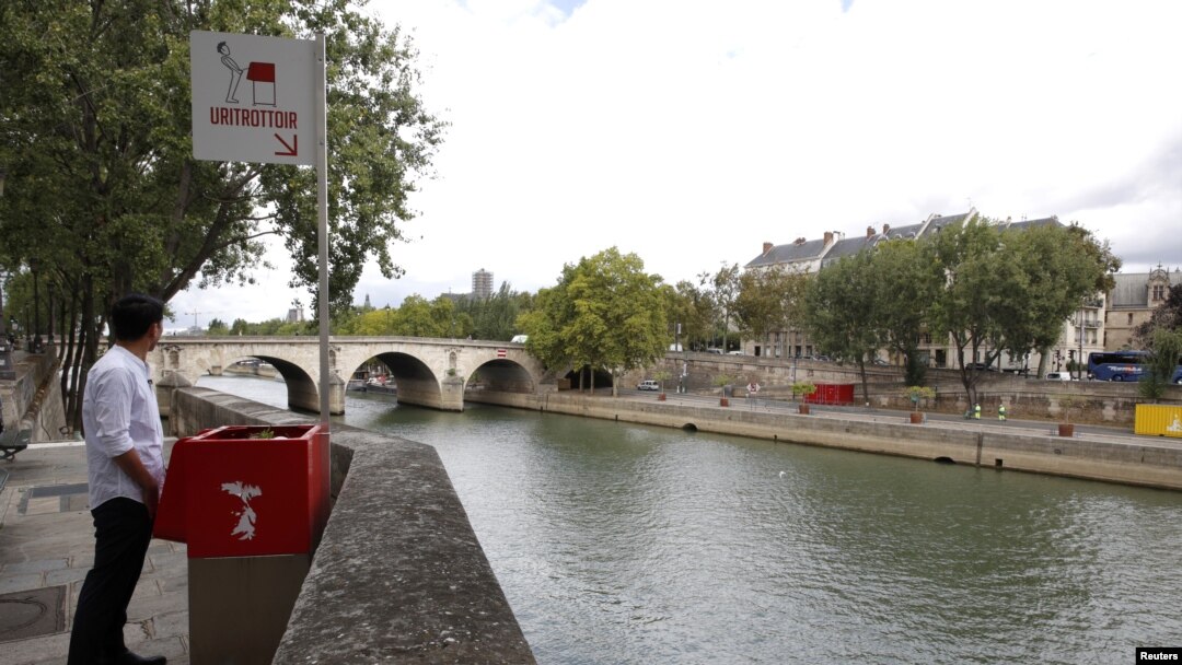 Seorang wartawan berpose di dekat tempat BAK ramah lingkungan yang dicat merah di Ile Saint-Louis di pinggiran Sungai Seine, Paris, Perancis, 13 Agustus 2018.
