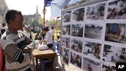 A Cambodian man, left, views photos the scene of victims of the March 30, 1997 deadly grenade attack, dispaying during a Buddhist ceremony in Phnom Penh, Cambodia, Wednesday, March 30, 2011. Buddhist monks and the main opposition party members in Cambodia