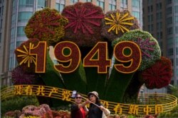 Chinese women take a selfie with a floral decoration with the words "Without the Communist Party, There would be no new China" in Beijing, June 28, 2021.