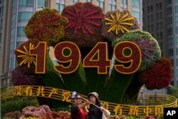 Chinese women take a selfie with a floral decoration with the words "Without the Communist Party, There would be no new China" in Beijing, June 28, 2021.