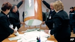 Local election commission officials empty a ballot box to count votes cast for the presidential elections at a polling station, as a police officer, right, looks on, in Tashkent, Uzbekistan, Sunday, Dec. 23, 2007. Uzbekistan's President Islam Karimov, a f