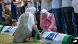 Dua orang perempuan menangis di tengah persiapan pemakaman korban yang baru diidentifikasi di pemakaman peringatan di Potocari dekat Srebrenica, Bosnia, Minggu, 11 Juli 2021. (Foto: AP)