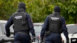 Police wearing balaclavas hold a battering ram used to break down a door outside the residence of internet influencer Andrew Tate during an early morning police search raid, on the outskirts of Bucharest, Romania, Aug. 21, 2024. 