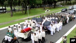 Imelda Marcos (mengenakan baju hitam di atas kursi roda, di bawah payung), janda mantan diktator Filipina Ferdinand Marcos, dan keluarga dekat mereka ikut dalam iring-iringan peti yang membawa jenazah Ferdinand Marcos yang akan dimakamkan di Taman Makam Pahlawan di kota Taguig, Filipina (18/11).