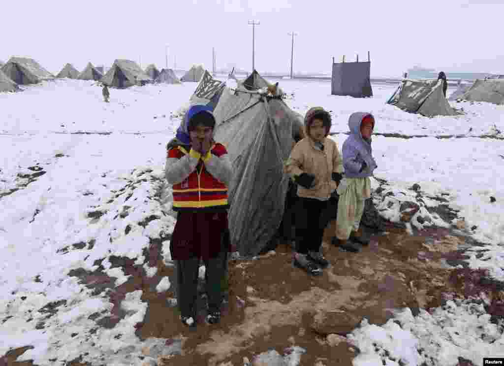 Internally displaced Afghan children stand outside their shelter in the cold at a refugee camp on the outskirts of Herat city.