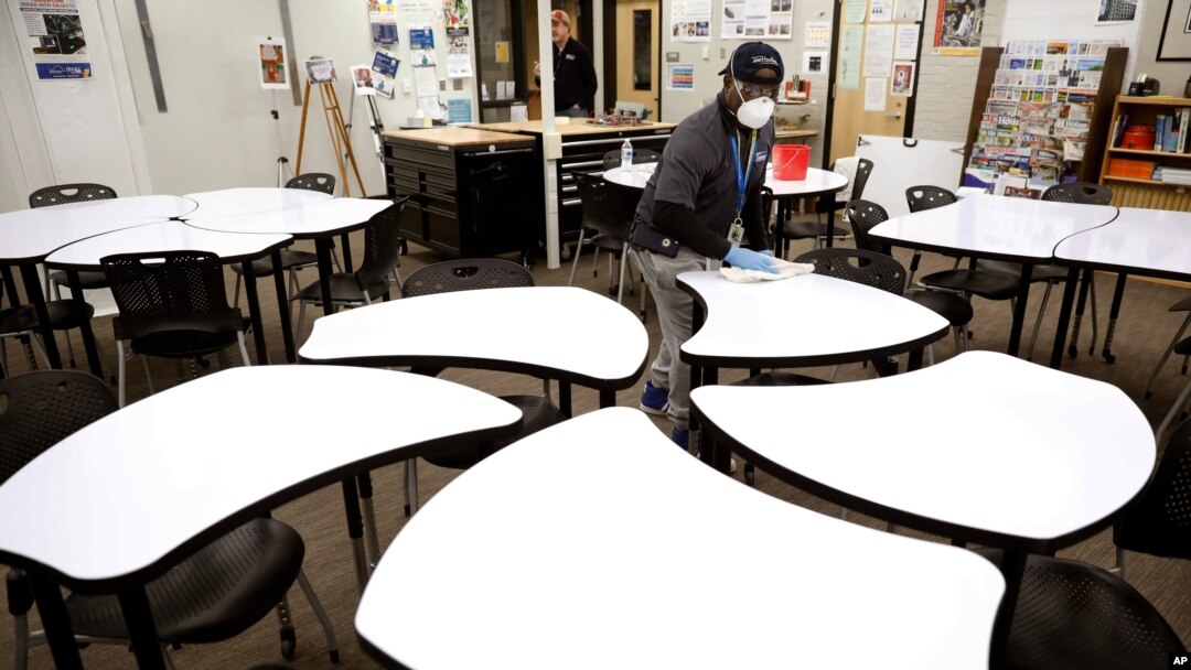 FILE - Des Moines Public School employee Sam Teah sanitizes a desk in a classroom at Central Campus high school in Des Moines, Iowa, March 19, 2020.