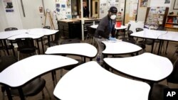 FILE - Des Moines Public School employee Sam Teah sanitizes a desk in a classroom at Central Campus high school in Des Moines, Iowa, March 19, 2020.