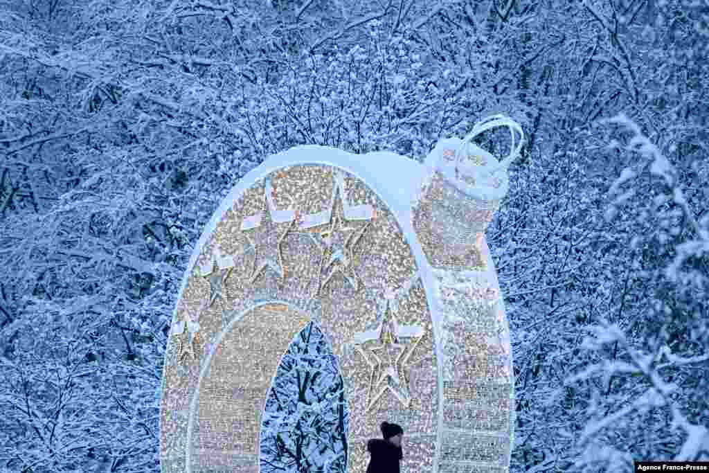 A woman walks past a light arch set up for the upcoming New Year and Christmas holidays in front of snow covered trees after heavy snowfall in Moscow outskirts, Russia.