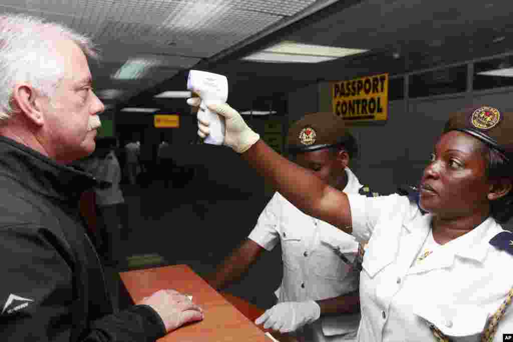 Petugas kesehatan di pelabuhan memeriksa suhu tubuh penumpang dengan termometer di gedung kedatangan di bandar udara internasional Murtala Mohammed di Lagos, Nigeria (20/10). (AP/Sunday Alamba)