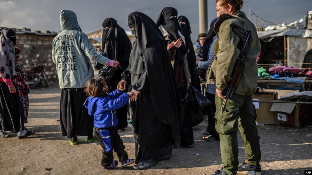FILE - Veiled women, reportedly wives and members of the Islamic State, walk under the supervision of a fighter from the Syrian Democratic Forces at the al-Hol camp in al-Hasakah governorate in northeastern Syria, Feb. 17, 2019.