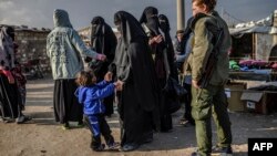 FILE - Veiled women, reportedly wives and members of the Islamic State, walk under the supervision of a fighter from the Syrian Democratic Forces at the al-Hol camp in al-Hasakah governorate in northeastern Syria, Feb. 17, 2019.