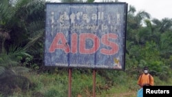 FILE - A man stands next to an AIDS billboard as he cleans a street in Yaounde, Cameroon, March 20, 2009. 