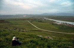 FILE - In this May 1, 2019, photo, a woman and child sit on a hill overlooking the Euphrates River in Derik, Syria. Turkey wants to establish a safe zone east of the Euphrates River in Syria.