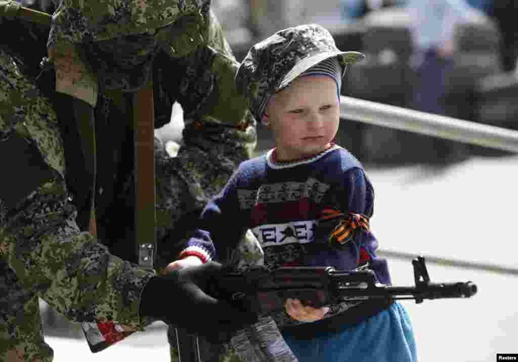 A pro-Russian armed man hands his weapon to a boy posing for a picture for his father in front of the seized town administration building in Kostyantynivka, April 28, 2014.