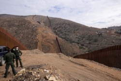 FILE - U.S. border patrol agents stand near the location of halted construction along the U.S. border wall with Mexico as an unfinished section is shown on Otay Mountain, east of San Diego, California, Feb. 2, 2021.