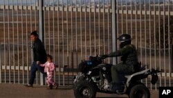 FILE – A migrant and her daughter walk along a secondary border fence in San Ysidro, California, after turning themselves in to U.S. border patrol agents after crossing the border wall from Playas de Tijuana, Mexico, Dec. 4, 2018. 