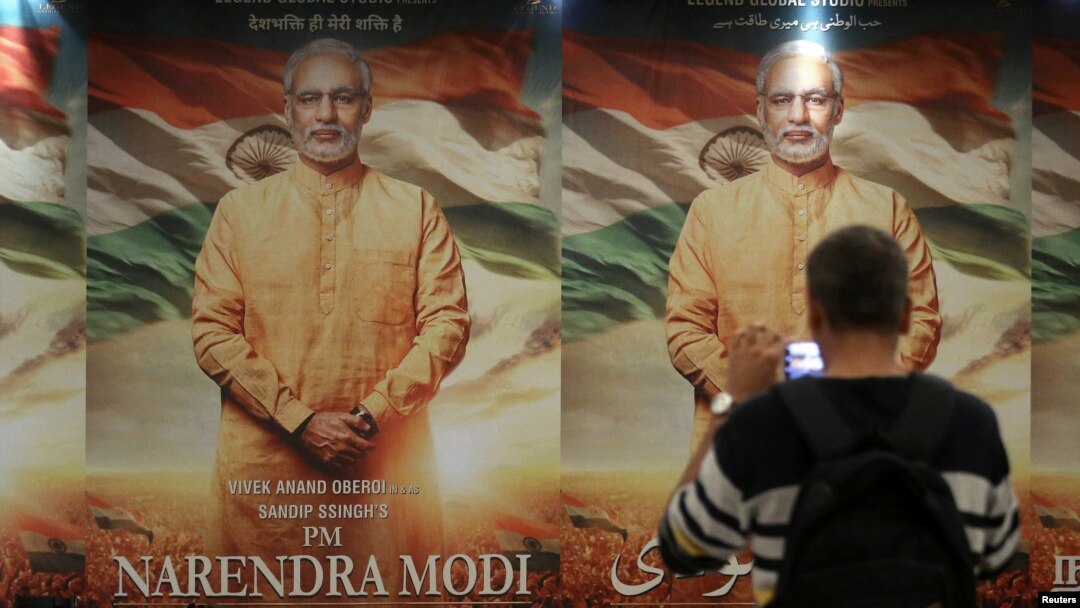 FILE - A man uses his mobile phone to take photos of a poster for the now delayed film "PM Narendra Modi" in Mumbai, India, Jan. 7, 2019.