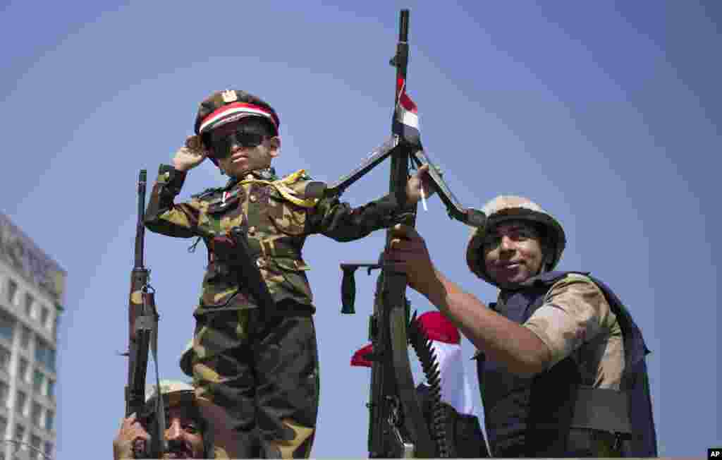 An Egyptian boy in an army costume salutes while posing next to army soldiers, from atop an armored vehicle guarding an entrance to Tahrir Square, Cairo, Oct. 6, 2013.