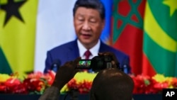 FILE - An African journalist films the screen at the media center showing China's President Xi Jinping delivering an opening ceremony speech for the China Africa Forum, at the Great Hall of the People in Beijing, Sept. 5, 2024. 