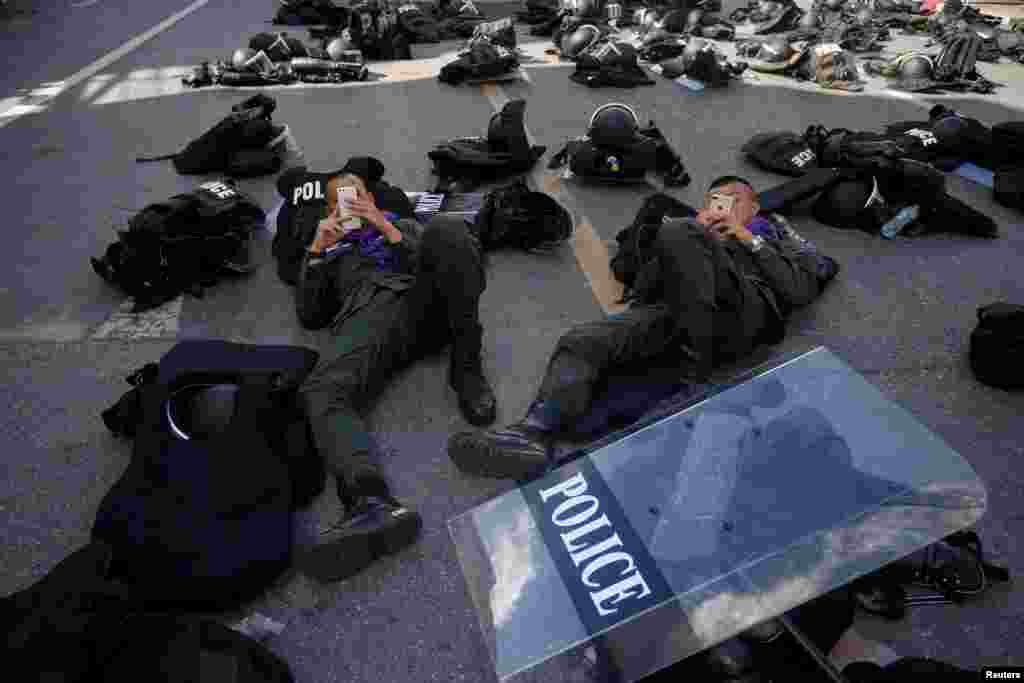 Police officers use their mobile phones near the Crown Property Bureau, ahead of a pro-democracy rally demanding Thailand&#39;s King Maha Vajiralongkorn hands back royal assets to the people and reforms on the monarchy, in Bangkok.