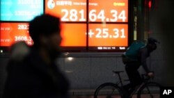 A man wearing a mask against the spread of the coronavirus rides a bicycle past an electronic stock board showing Japan's Nikkei 225 index at a securities firm in Tokyo, Jan. 12, 2021. 