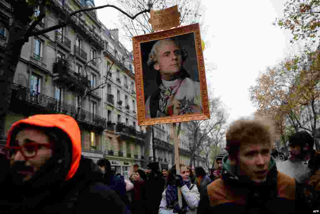 A woman holds a portrait of French President Emmanuel Macron painted as a royalty with a sign on top of it reading &quot;14 mai 2017 restoration of the monarchy&quot; during a demonstration against the pension overhauls, in Paris.