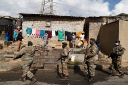 People stand near their home and watch as members of the South African Defence Force patrol their area in Alexandra township, Johannesburg. Stores and warehouses in South Africa were hit by looters on July 13.