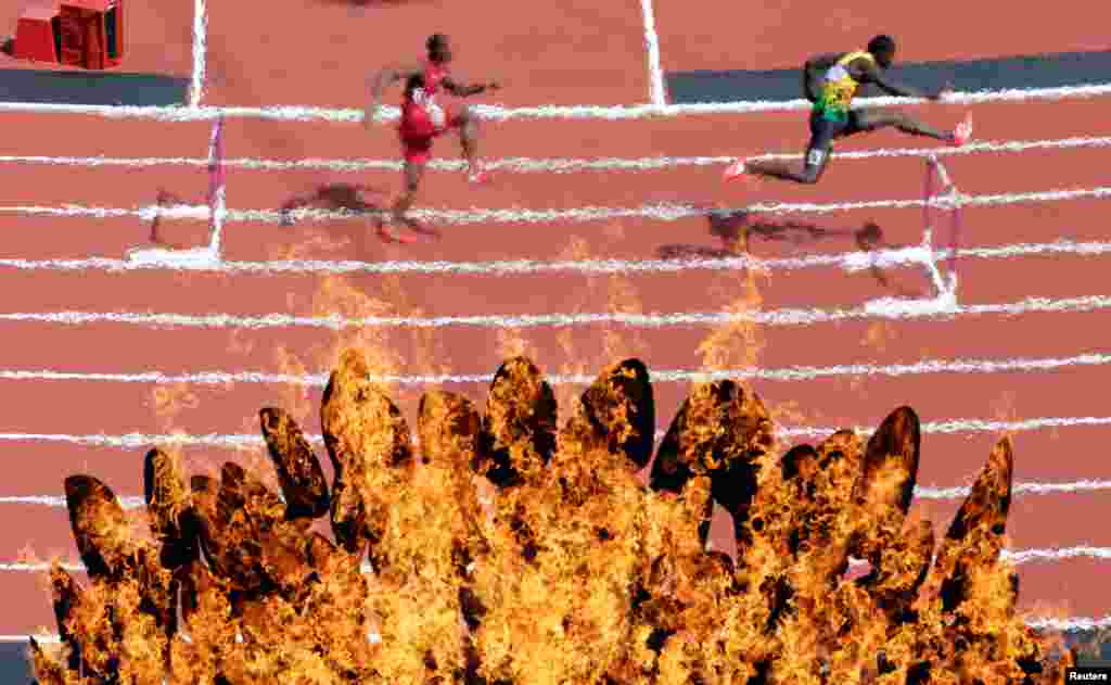 The Olympic flame burns while athletes compete in the men's 400m hurdles heats.