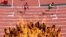 The Olympic flame burns while athletes compete in the men's 400m hurdles heats.