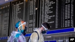 Passengers with protection gear walk past the flight board at the airport in Frankfurt, Germany, Friday, July 24, 2020. (AP Photo/Michael Probst)