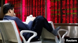 An investor reads a newspaper in front of an electronic board showing stock information at a brokerage house in Beijing, China, Feb. 16, 2016.