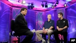 FILE - Greg Gumbel, left, watches as Connecticut head coach Jim Calhoun talks to Butler head coach Brad Stevens, right, prior to taping a television interview in Houston, Texas, April 3, 2011.