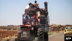 A Syrian family rides with belongings on a tractor-drawn trailer as they flee from fighting in the southern Syrian province of Daraa, June 21, 2018.