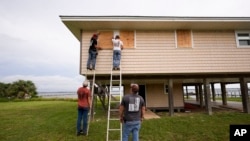 Jerry McCullen, top of ladder left, and Carson Baze, top of ladder right, put plywood over the windows of a house ahead of Hurricane Helene, expected to make landfall Thursday evening, in Alligator Point, Florida, Sept. 25, 2024.