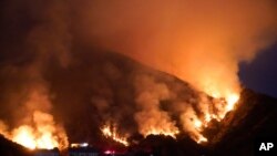 The Ranch Fire burns over a residential area, Aug. 13, 2020, in Azusa, California. Heat wave conditions were making difficult work for fire crews battling brush fires and wildfires across Southern California.