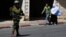 Palestinians walk near an Israeli soldier as he stands guard during an operation to locate three Israeli teens in the West Bank City of Hebron, June 17, 2014.